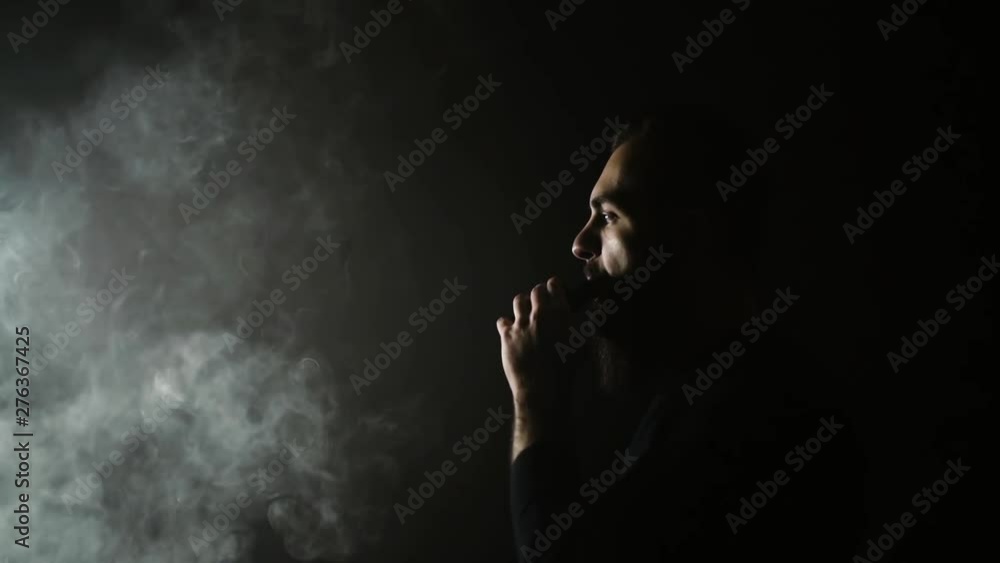 Portrait of bearded man standing in profile and exhales thick white steam through his mouth on isolated black background in slow motion in professional dark studio. Guy leaves after his stunt. Portrait of bearded man standing in profile and exhales thick white steam through his mouth on isolated black background in slow motion in professional dark studio. Guy leaves after his stunt.