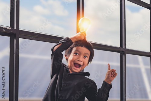 Child with future of alternative energy and sustainable energy. Funny Asian boys hold a light bulb that shines in their hands at Solar panel, photovoltaic. Eco-Friendly and Pure energy Concept