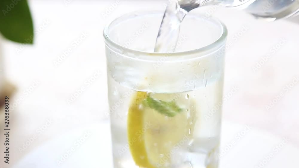 Pouring a glass of water with lemon, ice and mint on a white table Selective focus HD video Slow motion Pouring a glass of water with lemon, ice and mint on a white table Selective focus HD video Slow motion