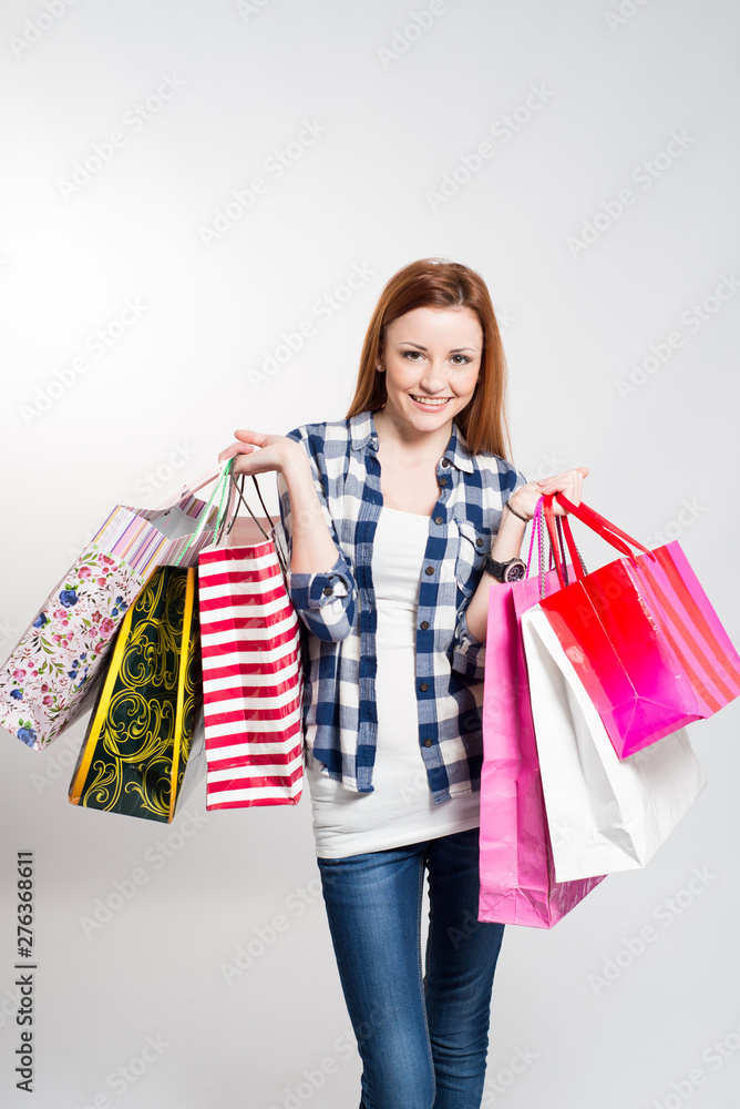 Young attractive smiling woman with many colored shopping bags on gray. Woman making shopping