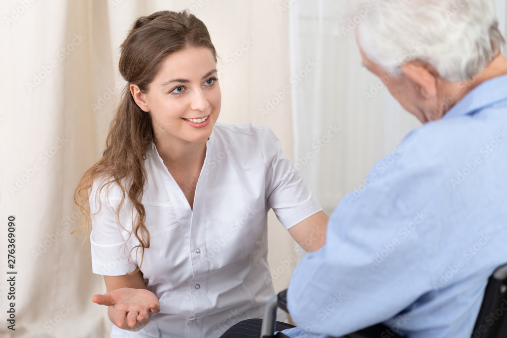 Fototapeta premium Young helpful doctor with senior man on wheelchair