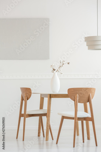 Closeup of flowers in white vase on wooden dining table with chairs
