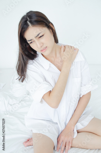 Asian women wear white pajamas in the bedroom. She has pain in the neck area.