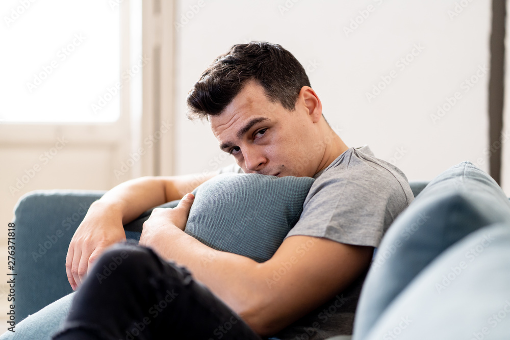 Young man suffering from depression lying on sofa alone at home feeling frustrated and hopeless Young man suffering from depression lying on sofa alone at home feeling frustrated and hopeless