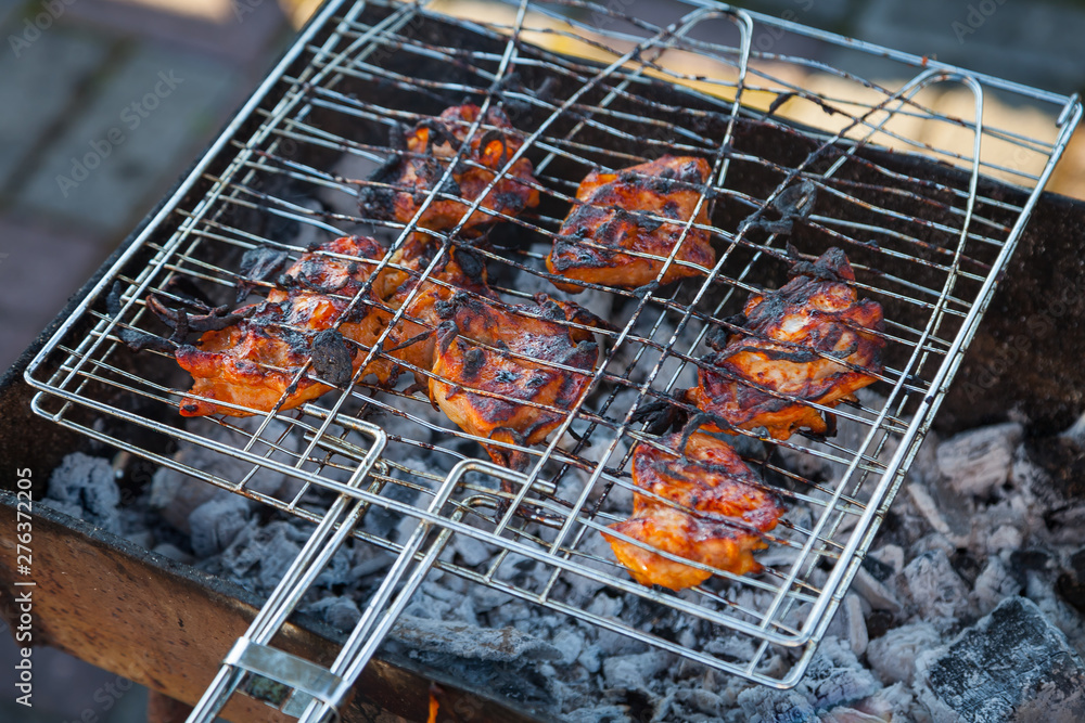 Close-up on the process of cooking shashlik of pork or beef meat clamped in a grill with a crispy burnt crust over gray burnt coals on an open fire