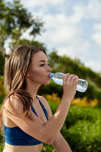 sportswoman drinks water from plastic bottle in the park after training