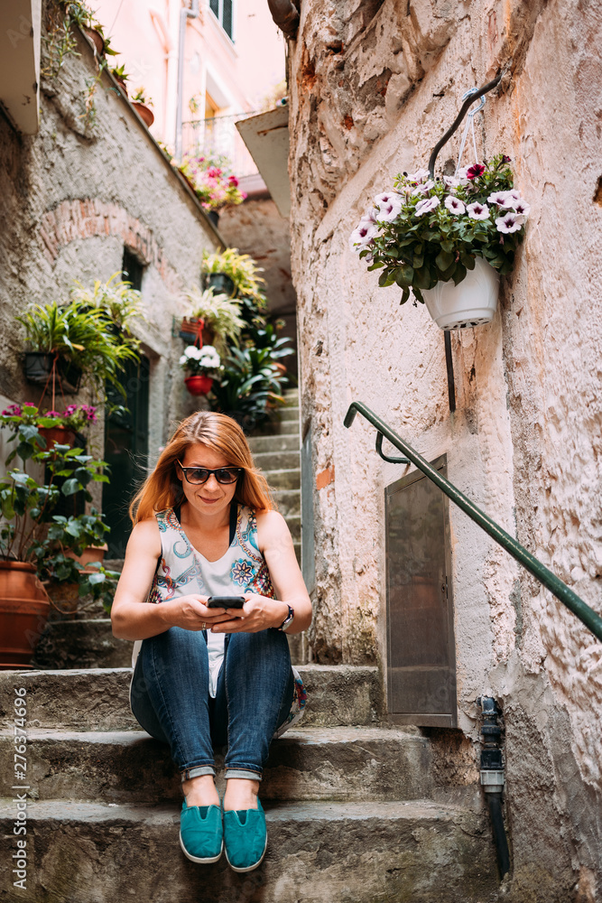 Young woman using smartphone sitting on the steps in an Italian village