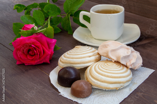 Delicate multicolored marshmallows on white openwork plate. Still life with marshmallows, a Cup of tea and a rose on vintage background.