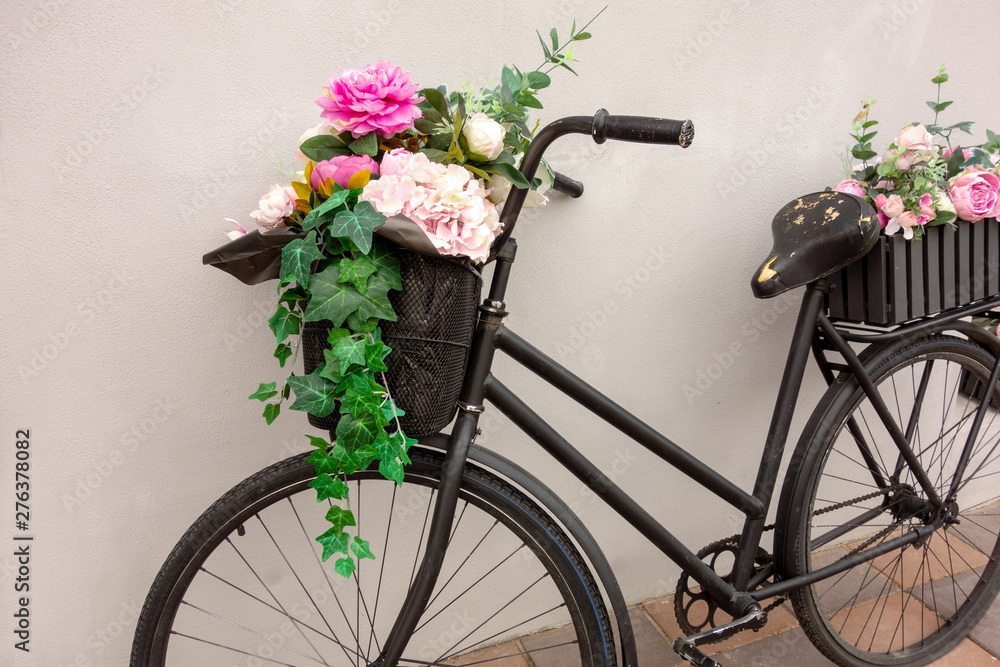 Retro bicycle as a flowerbed decoration outside element. Black aged bike stays against the wall with two garden baskets with beauty flowers. Art decor closeup macro