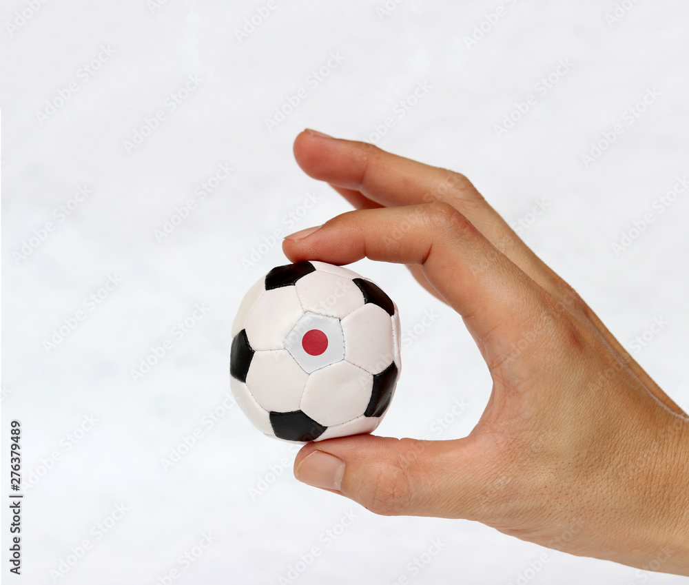 Mini ball of football in hand and one black point of football is Japan flag, hold it with two finger on white background. Mini ball of football in hand and one black point of football is Japan flag, hold it with two finger on white background.