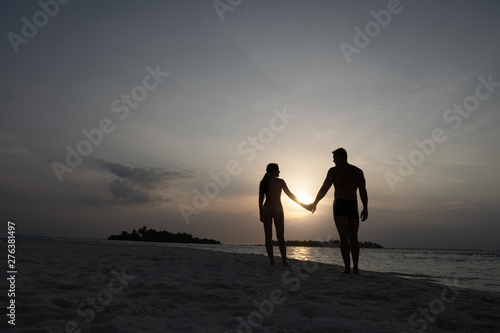 Love couple holding hands at sunset. Silhouettes of a guy and a girl on the background of the sun