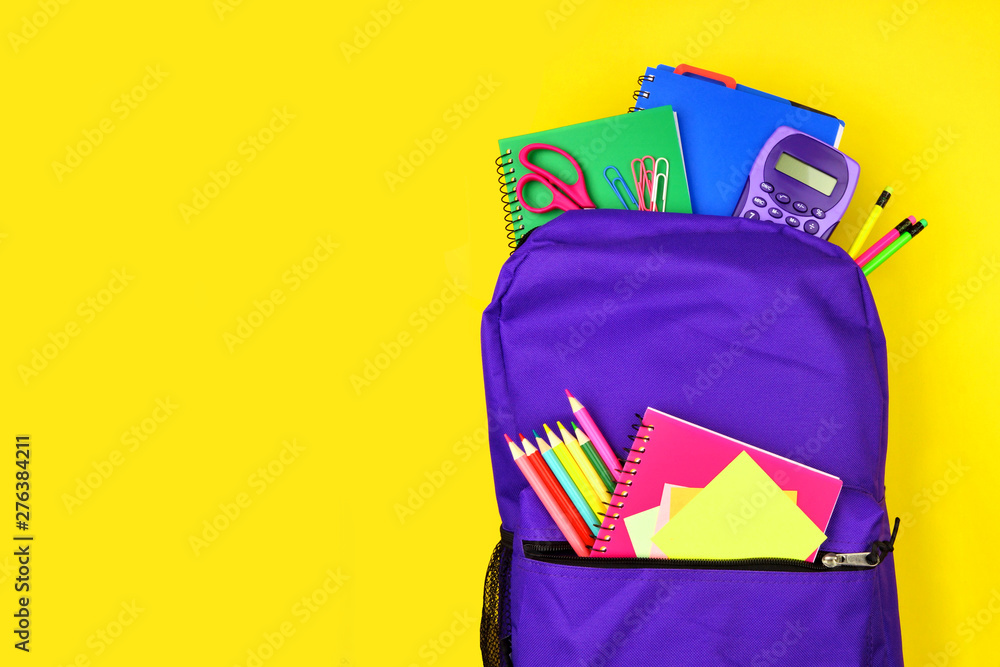 Purple backpack full of school supplies against a bright yellow background. Close up, top view with copy space. - obrazy, fototapety, plakaty 