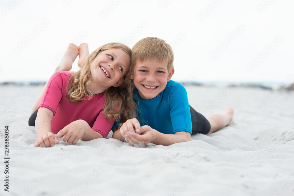Portrait of two happy children in neoprene swimsuits playing on the beach with sand Portrait of two happy children in neoprene swimsuits playing on the beach with sand