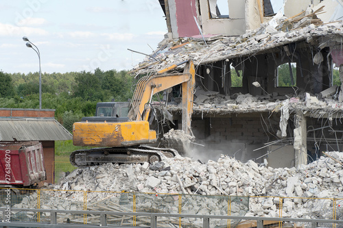 Yellow excavator picks up construction waste for loading onto a truck. Technique destroyed the building, is reinforcement, concrete and stones. Destroyed house, concrete, fittings, dust flies. Similia