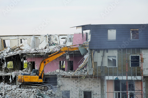 A yellow excavator demolishes a multi-storey building with a ladle. Technique destroys the building  is fittings  concrete and stones. Destroyed house  broken floors  destroyed the walls and roof. Sim