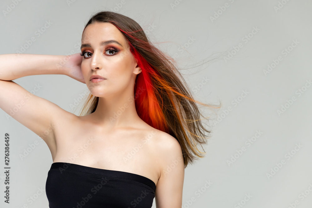Fototapeta premium A close-up portrait photo of a fashionable hairstyle red-yellow in studio on a white background. The pretty brunette model with beautiful make-up has beautiful flowing colorful hair.