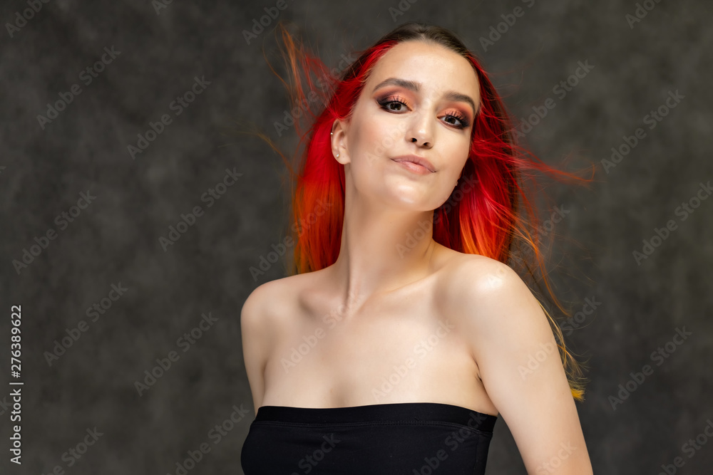 A close-up portrait photo of a fashionable hairstyle red-yellow in studio on a gray background. The pretty brunette model with beautiful make-up has beautiful flowing colorful hair. A close-up portrait photo of a fashionable hairstyle red-yellow in studio on a gray background. The pretty brunette model with beautiful make-up has beautiful flowing colorful hair.
