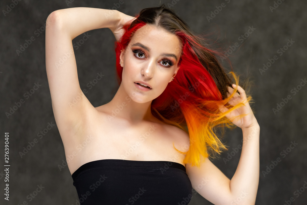 A close-up portrait photo of a fashionable hairstyle red-yellow in studio on a gray background. The pretty brunette model with beautiful make-up has beautiful flowing colorful hair. A close-up portrait photo of a fashionable hairstyle red-yellow in studio on a gray background. The pretty brunette model with beautiful make-up has beautiful flowing colorful hair.