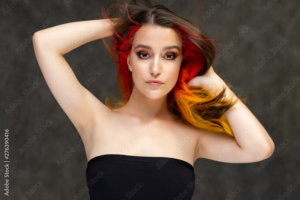 A close-up portrait photo of a fashionable hairstyle red-yellow in studio on a gray background. The pretty brunette model with beautiful make-up has beautiful flowing colorful hair. A close-up portrait photo of a fashionable hairstyle red-yellow in studio on a gray background. The pretty brunette model with beautiful make-up has beautiful flowing colorful hair.