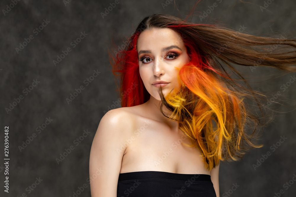 A close-up portrait photo of a fashionable hairstyle red-yellow in studio on a gray background. The pretty brunette model with beautiful make-up has beautiful flowing colorful hair. A close-up portrait photo of a fashionable hairstyle red-yellow in studio on a gray background. The pretty brunette model with beautiful make-up has beautiful flowing colorful hair.