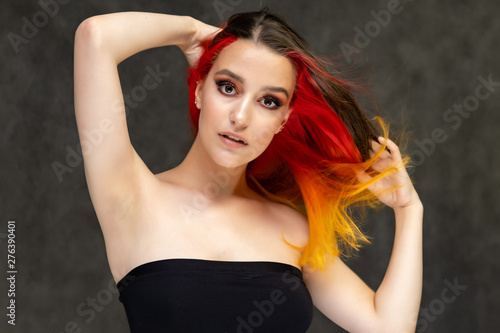 A close-up portrait photo of a fashionable hairstyle red-yellow in studio on a gray background. The pretty brunette model with beautiful make-up has beautiful flowing colorful hair. © Вячеслав Чичаев