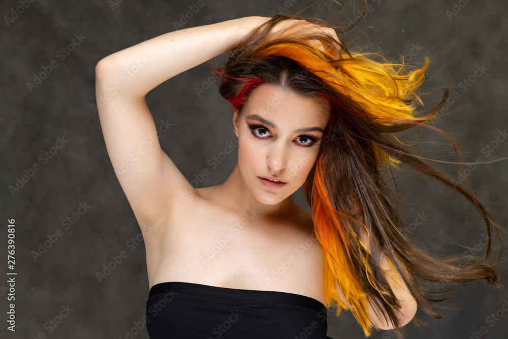 A close-up portrait photo of a fashionable hairstyle red-yellow in studio on a gray background. The pretty brunette model with beautiful make-up has beautiful flowing colorful hair. A close-up portrait photo of a fashionable hairstyle red-yellow in studio on a gray background. The pretty brunette model with beautiful make-up has beautiful flowing colorful hair.