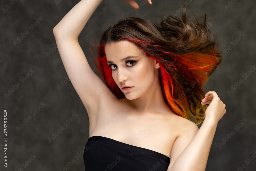 Naklejka premium A close-up portrait photo of a fashionable hairstyle red-yellow in studio on a gray background. The pretty brunette model with beautiful make-up has beautiful flowing colorful hair.