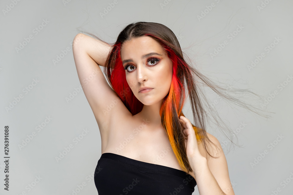 A close-up portrait photo of a fashionable hairstyle red-yellow in studio on a blue background. The pretty brunette model with beautiful make-up has beautiful flowing colorful hair. A close-up portrait photo of a fashionable hairstyle red-yellow in studio on a blue background. The pretty brunette model with beautiful make-up has beautiful flowing colorful hair.