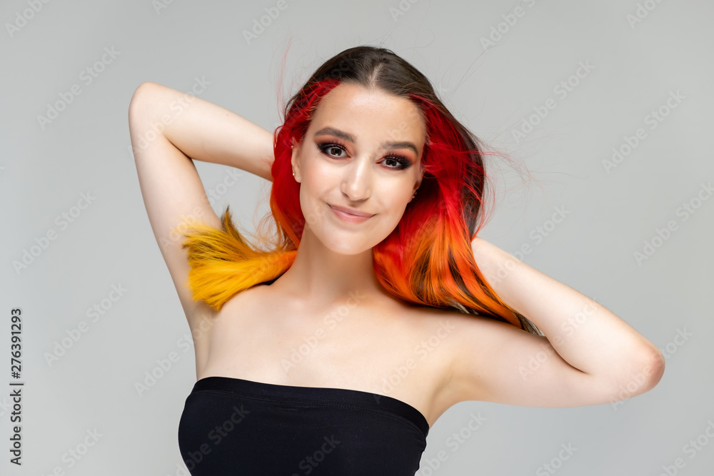 A close-up portrait photo of a fashionable hairstyle red-yellow in studio on a blue background. The pretty brunette model with beautiful make-up has beautiful flowing colorful hair. A close-up portrait photo of a fashionable hairstyle red-yellow in studio on a blue background. The pretty brunette model with beautiful make-up has beautiful flowing colorful hair.