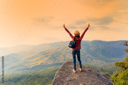 Happy standing on a rock with raised hands and looking at the valley below in Phu Lom Lo mountain, Loei, Thailand.