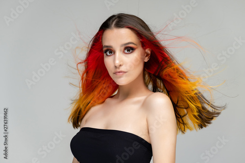 A close-up portrait photo of a fashionable hairstyle red-yellow in studio on a blue background. The pretty brunette model with beautiful make-up has beautiful flowing colorful hair.