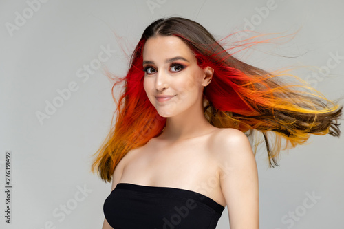 A close-up portrait photo of a fashionable hairstyle red-yellow in studio on a blue background. The pretty brunette model with beautiful make-up has beautiful flowing colorful hair.