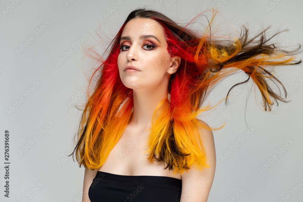 A close-up portrait photo of a fashionable hairstyle red-yellow in studio on a blue background. The pretty brunette model with beautiful make-up has beautiful flowing colorful hair. A close-up portrait photo of a fashionable hairstyle red-yellow in studio on a blue background. The pretty brunette model with beautiful make-up has beautiful flowing colorful hair.