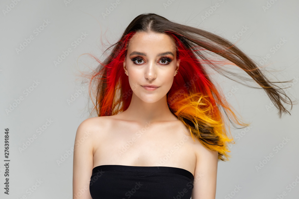 A close-up portrait photo of a fashionable hairstyle red-yellow in studio on a blue background. The pretty brunette model with beautiful make-up has beautiful flowing colorful hair. A close-up portrait photo of a fashionable hairstyle red-yellow in studio on a blue background. The pretty brunette model with beautiful make-up has beautiful flowing colorful hair.