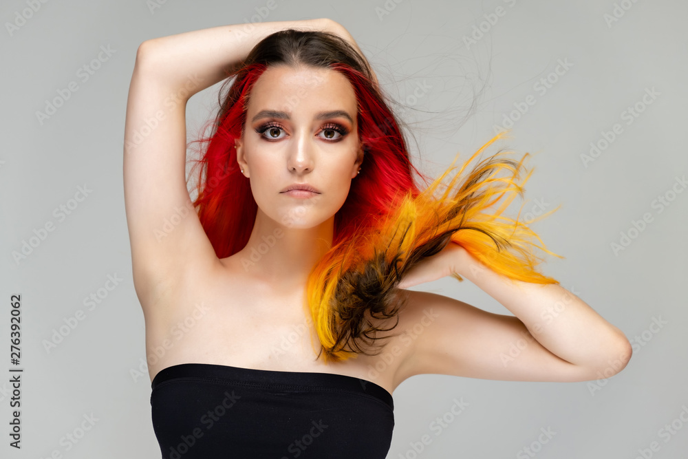 A close-up portrait photo of a fashionable hairstyle red-yellow in studio on a blue background. The pretty brunette model with beautiful make-up has beautiful flowing colorful hair. A close-up portrait photo of a fashionable hairstyle red-yellow in studio on a blue background. The pretty brunette model with beautiful make-up has beautiful flowing colorful hair.