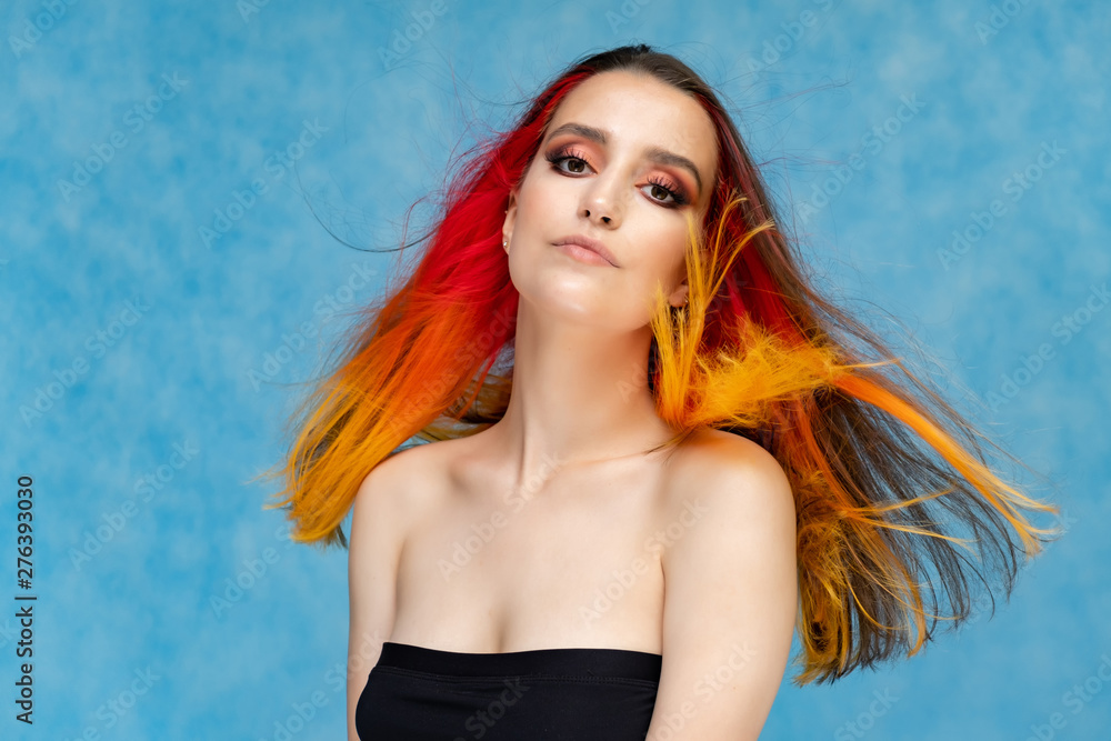 A close-up portrait photo of a fashionable hairstyle red-yellow in studio on a blue background. The pretty brunette model with beautiful make-up has beautiful flowing colorful hair. A close-up portrait photo of a fashionable hairstyle red-yellow in studio on a blue background. The pretty brunette model with beautiful make-up has beautiful flowing colorful hair.