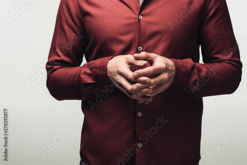partial view of man standing with clenched hands isolated on grey, human emotion and expression concept