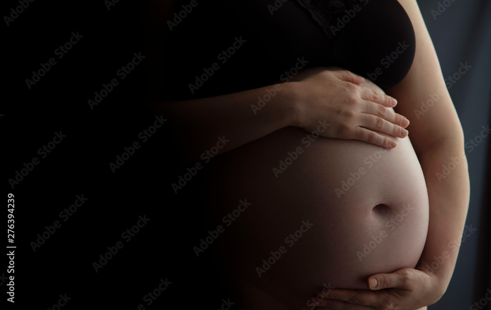 Pregnant woman holding a baby bump against a dark background Pregnant woman holding a baby bump against a dark background