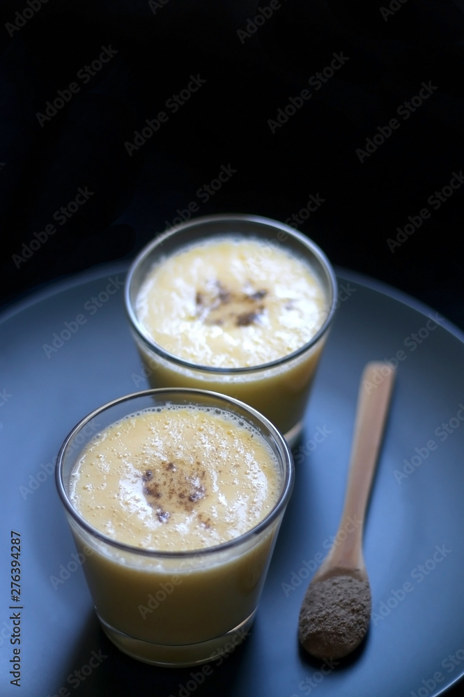 Two glasses of refreshing mango lassi drink, decorated with cardamom. Dark background, selective focus. Two glasses of refreshing mango lassi drink, decorated with cardamom. Dark background, selective focus.