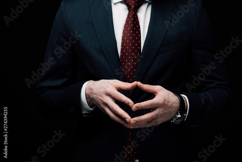 фотографія partial view of confident businessman showing steeple gesture isolated on black,