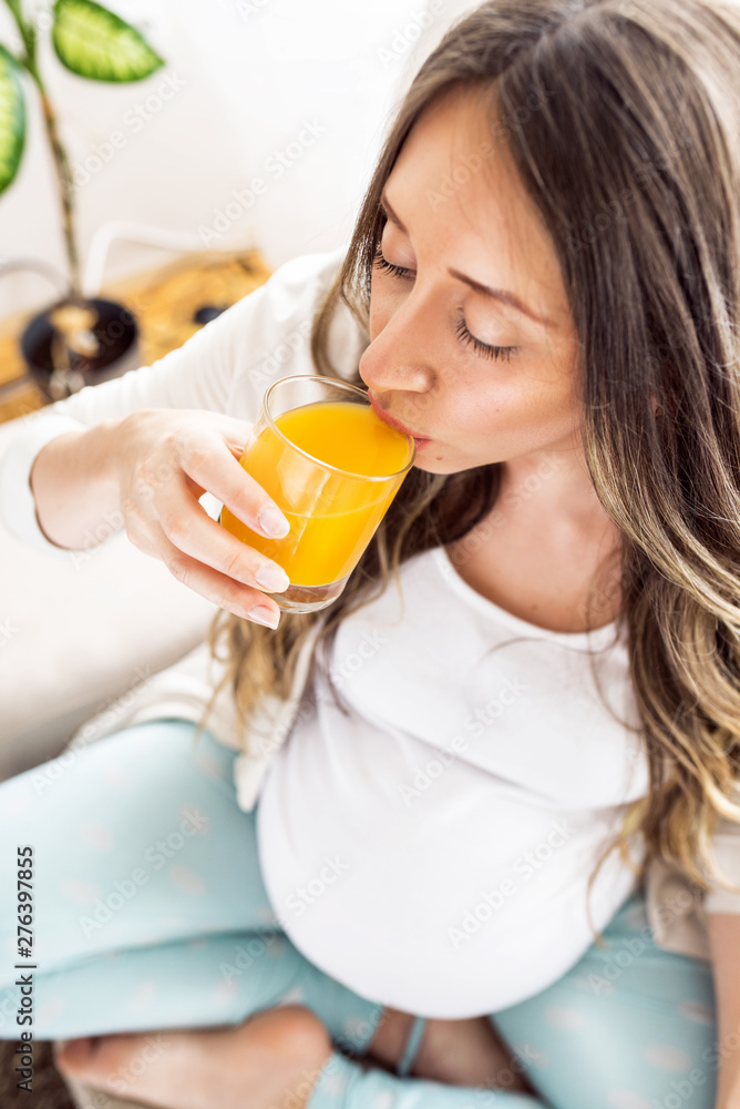 Happy smiling elegant pregnant woman drinking juice smoothie at home by window in living room. Happy smiling elegant pregnant woman drinking juice smoothie at home by window in living room.