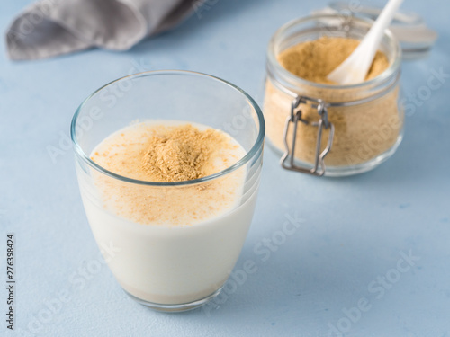 Nutritional yeast and milk. Nutritional inactive yeast in jar and glass of milk on blue tabletop. Copy space. Nutritional yeast is vegetarian superfood with cheese flavor, for healthy diet