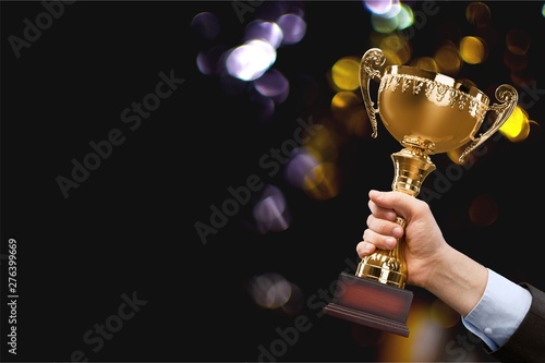 Close-up human hand holding golden Trophy on blurred background