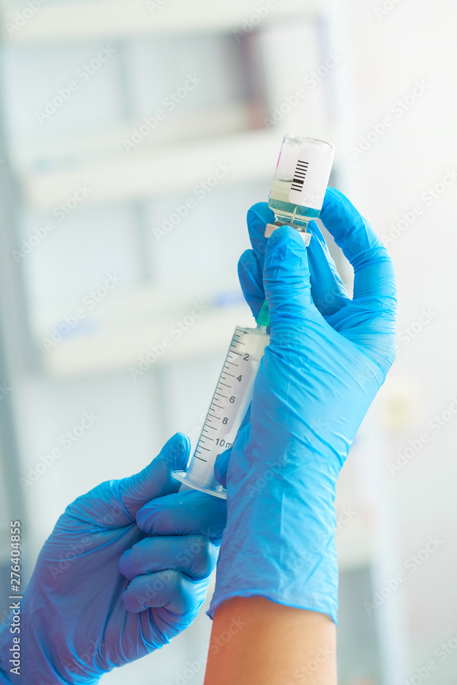 Nurse holding a medical syringe in hand and putting medicine inside it close-up. Injection preparation in hospital.