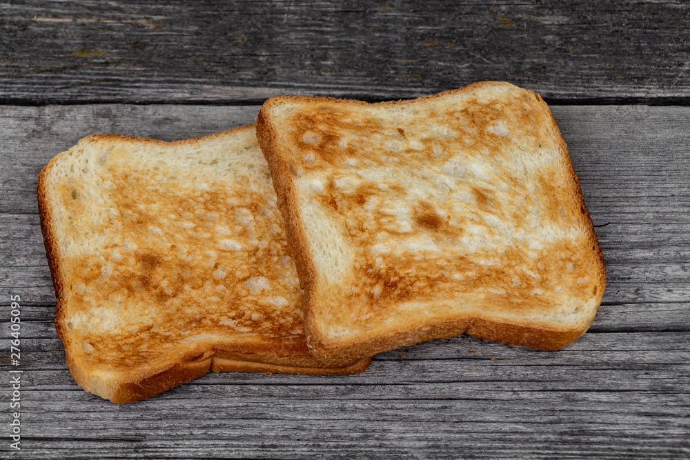 Two square ruddy pieces of bread for toasts on the old gray wooden background Two square ruddy pieces of bread for toasts on the old gray wooden background