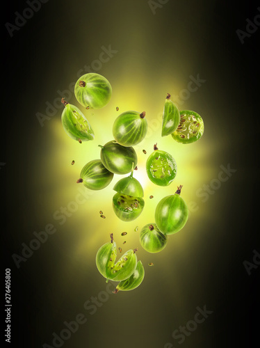 Whole and sliced fresh gooseberries in the air with flash of light in the dark