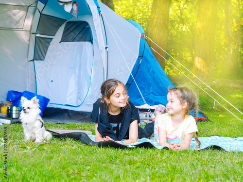 Camp in the tent - girls with little dog chihuahua sitting together near the tent. Camping with children. Camping tourism and vacation concept