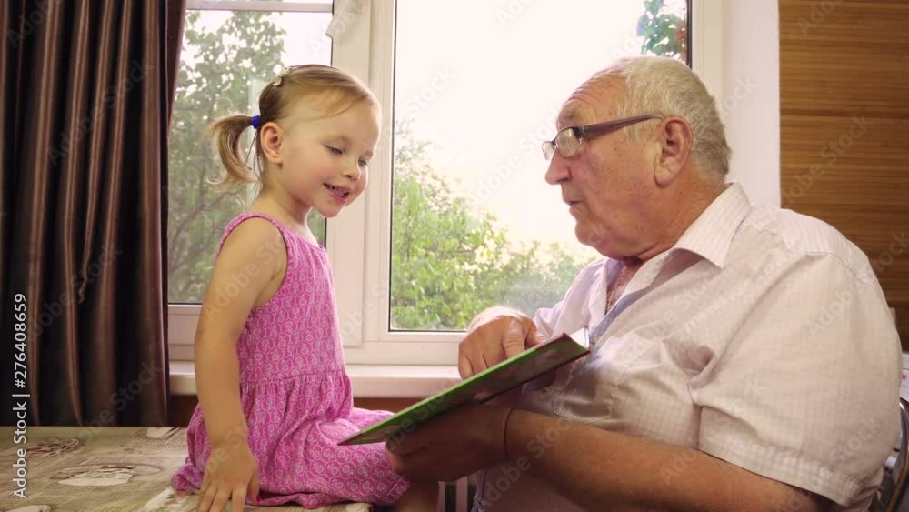 A little two-year-old girl plays with her happy grandfather. Read the book. A little two-year-old girl plays with her happy grandfather. Read the book.
