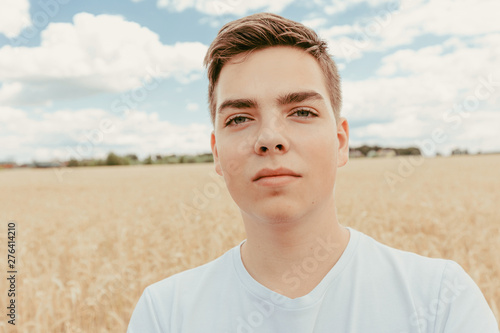 Portrait of handsome teenage boy outdoors, in front of wheat field, at summer day.