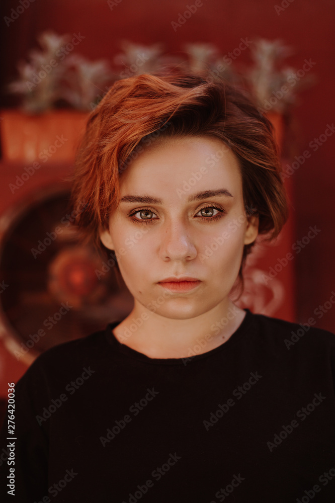 Portrait of attractive cheeky woman with short red hair at back yard in the old city with red walls Portrait of attractive cheeky woman with short red hair at back yard in the old city with red walls